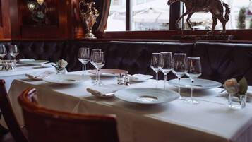 Un restaurante con mantel blanco, asientos tipo banca de cuero y una estatua decorativa de un caballo junto a la ventana.