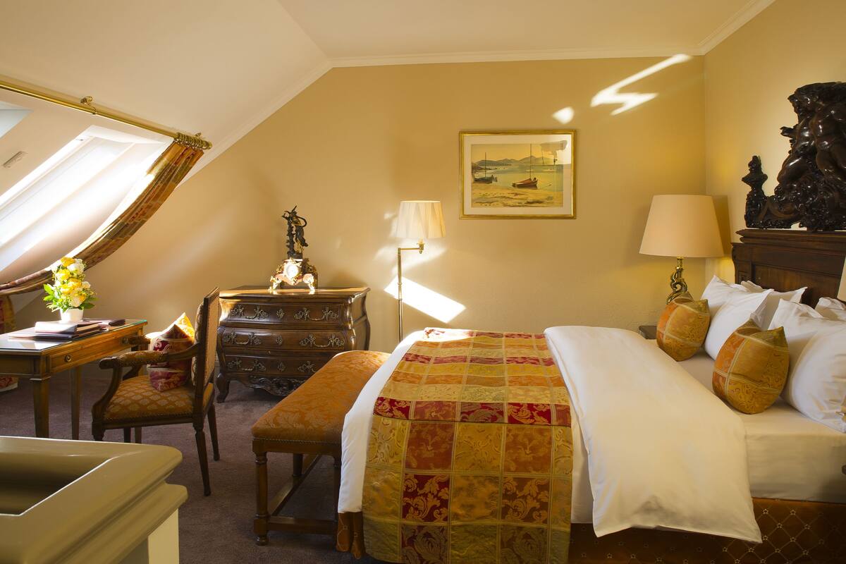 A hotel room with a bed, a desk, a chair, a dresser, and a lamp.