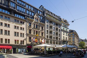 A hotel with multiple floors, outdoor seating, and flags. - Hôtel de La Cigogne (Geneva)
