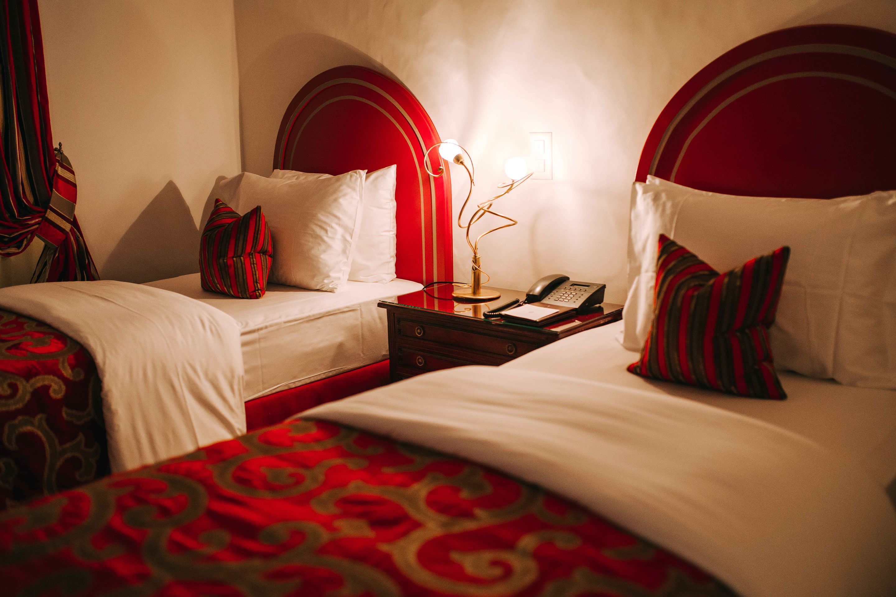 A hotel room with two beds, each with a red and white headboard, and a bedside table with a lamp and a telephone.