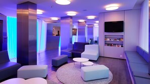A modern lounge area with sofas, a flat-screen TV, and a bookshelf. - Hotel Cristal (Geneva)