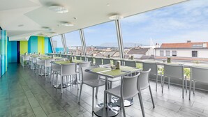 A modern outdoor dining area with white tables and chairs, large windows offering a city view. - Hotel Cristal (Geneva)