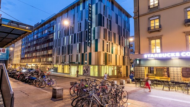 A modern hotel with a prominent sign, a Starbucks across the street, and bicycles parked outside. - Hotel Cristal (Geneva)