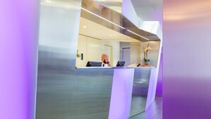 A modern reception desk with a glass partition, a computer, and a vase with flowers. - Hotel Cristal (Geneva)