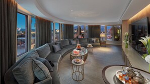 Una habitación de hotel moderna con un sofá curvo, una mesa de centro de cristal y una mesa de comedor con una bandeja de bebidas y un hervidor de té.