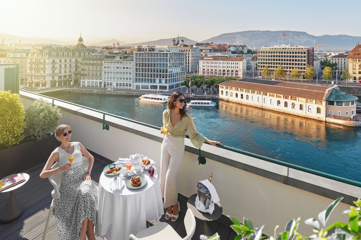 A terrace with a table set for breakfast, overlooking a river with boats and buildings in the background.