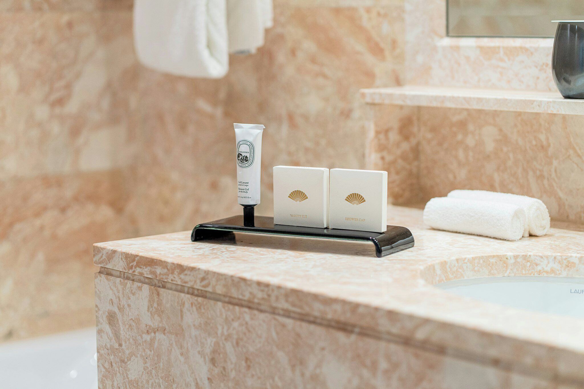 Une salle de bain avec un comptoir en marbre, une serviette, un bonnet de douche et un flacon de lotion.