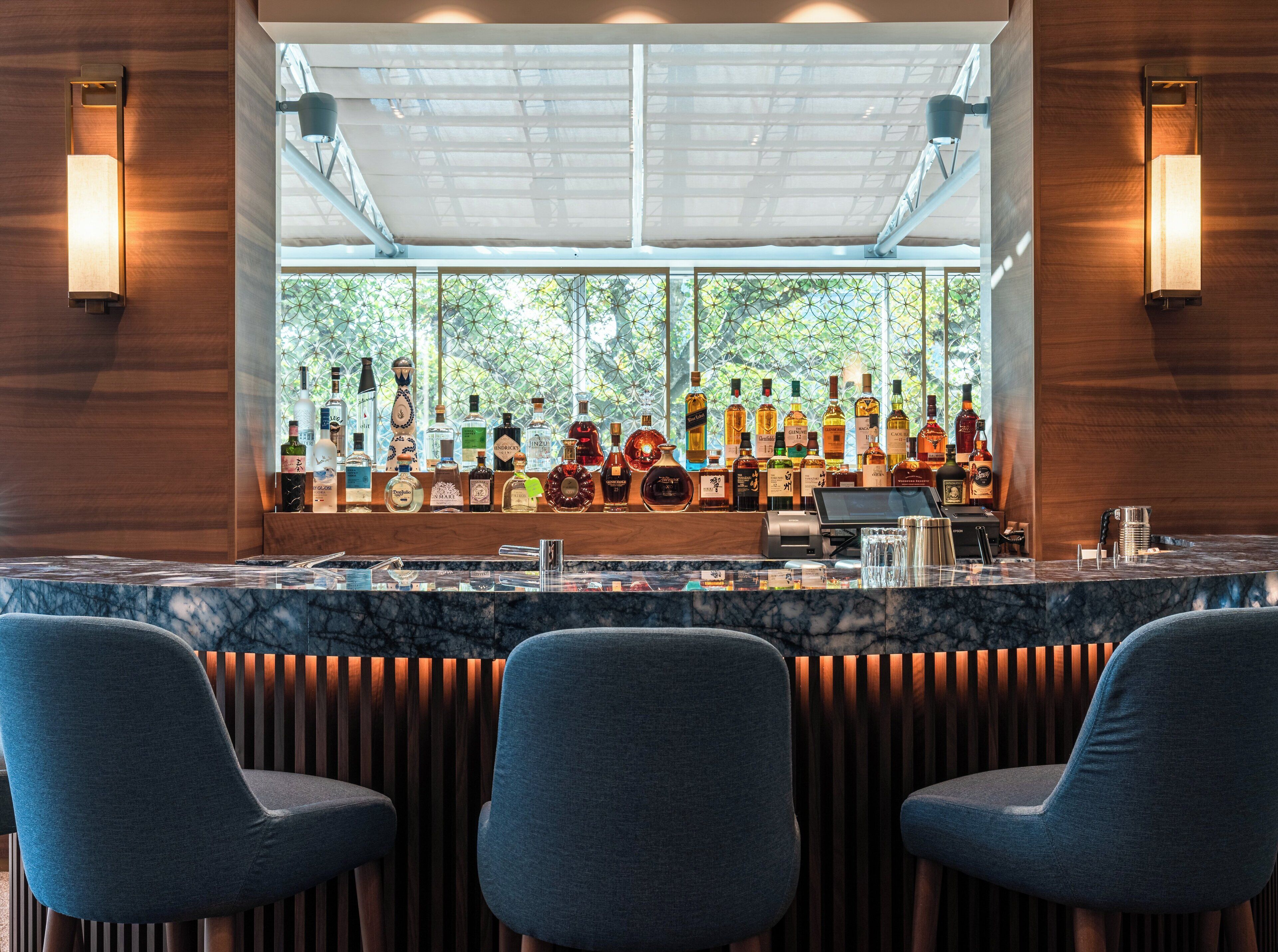 Un espace bar doté d’un comptoir en marbre, de plusieurs bouteilles d’alcool et de trois tabourets de bar.