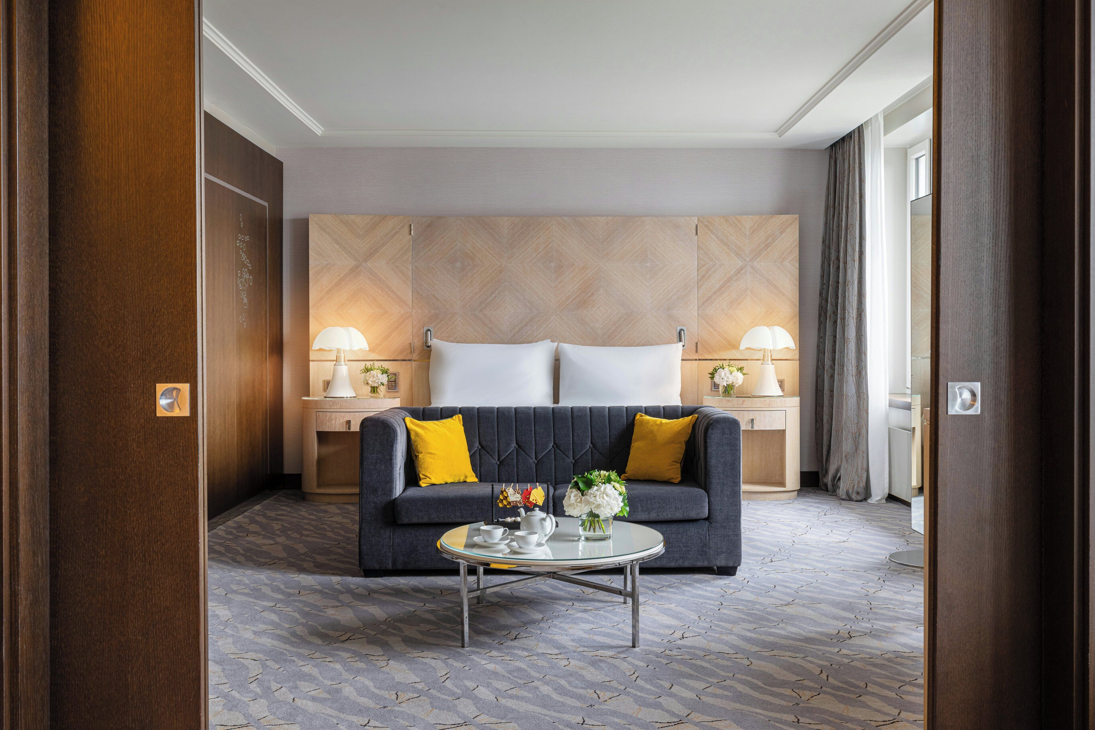 A hotel room with a sofa, two lamps, a coffee table, and a patterned carpet.
