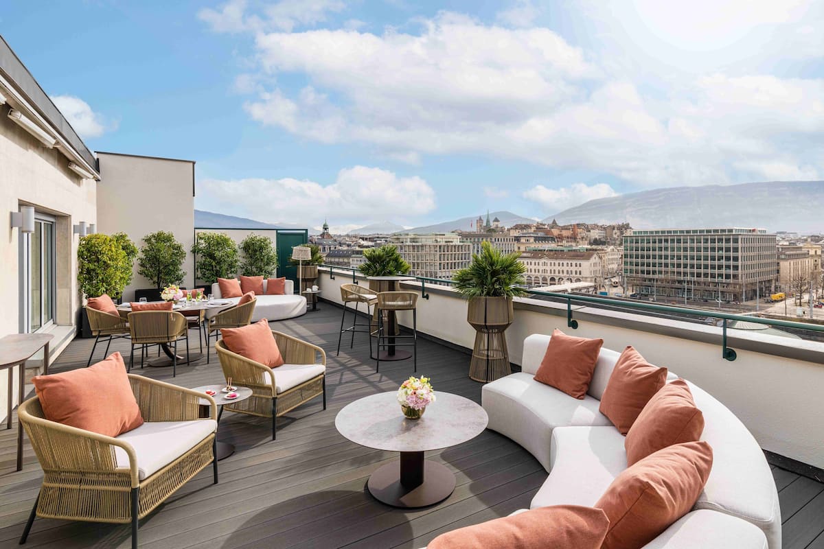 Una terraza en la azotea con mobiliario de mimbre, una mesa redonda con un centro de mesa floral y un sofá blanco con cojines.