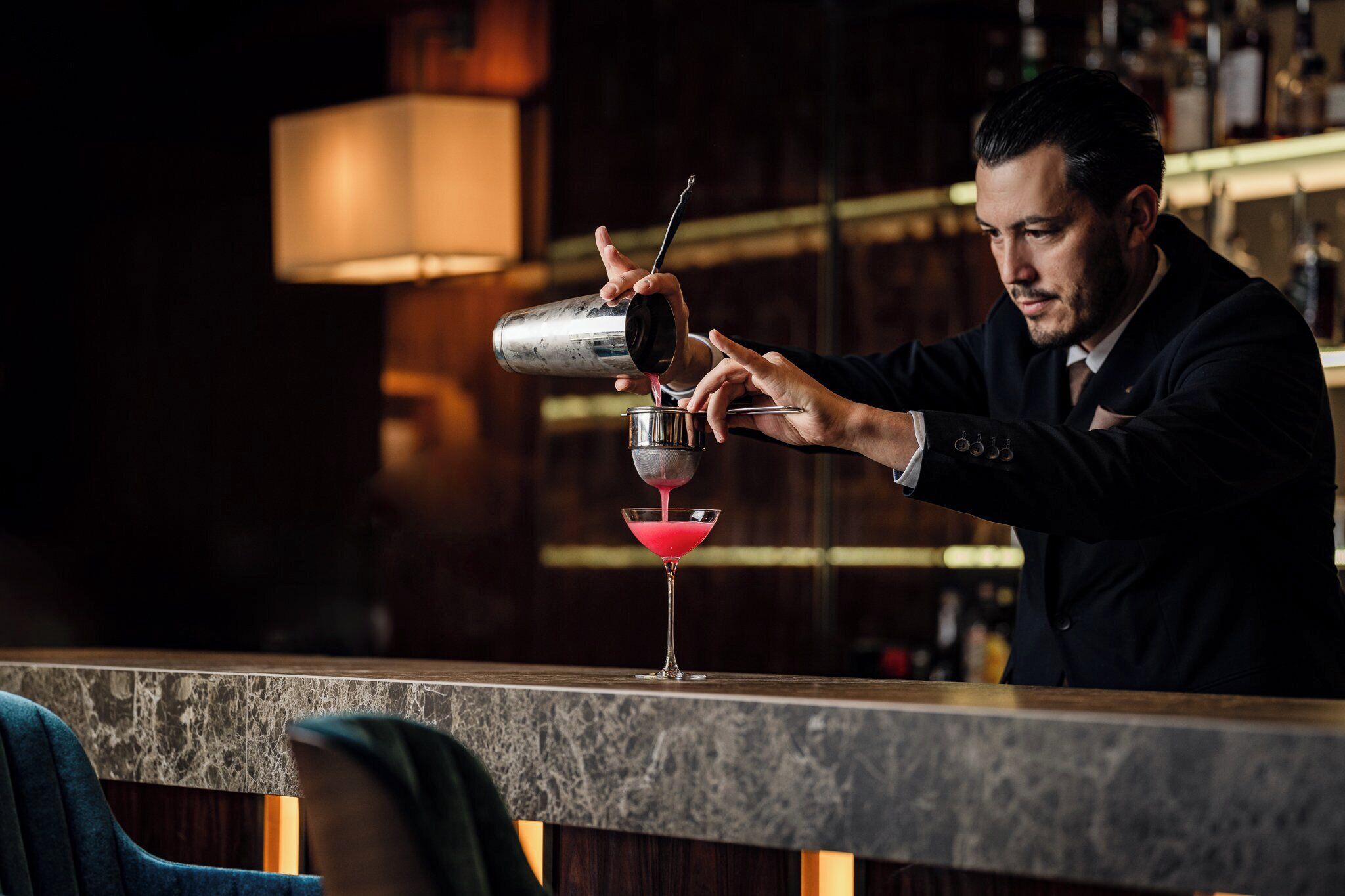 Un bartender sirviendo una bebida en una copa de martini.