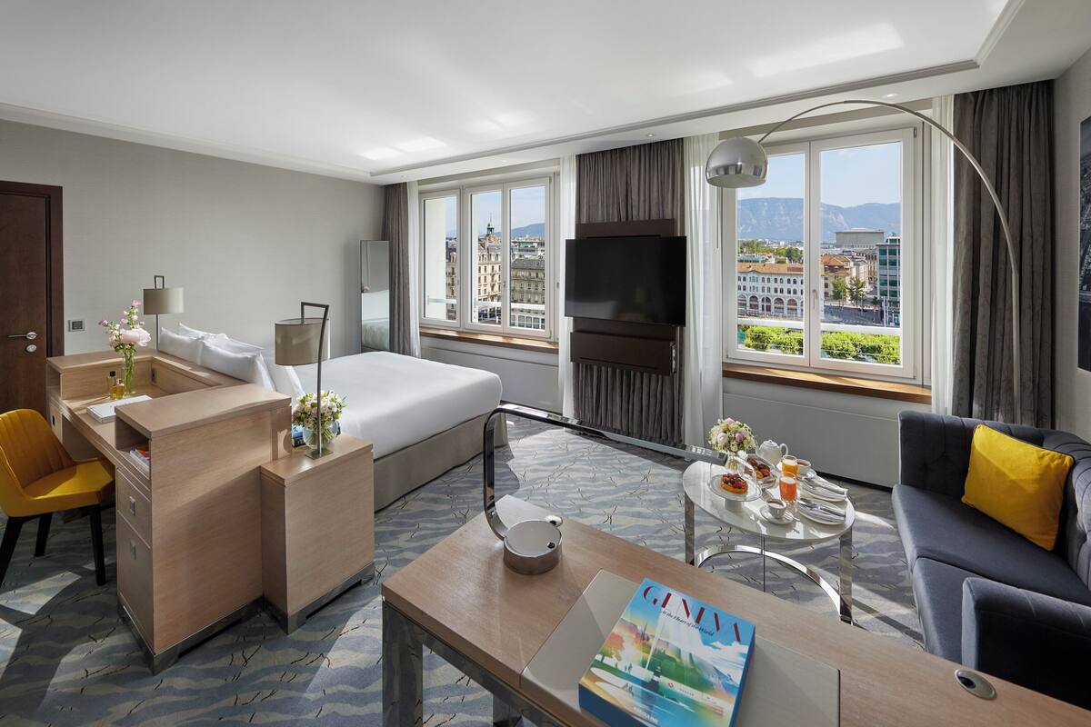 Una habitación de hotel con cama, escritorio, sofá, televisión y ventana con vista a la ciudad.