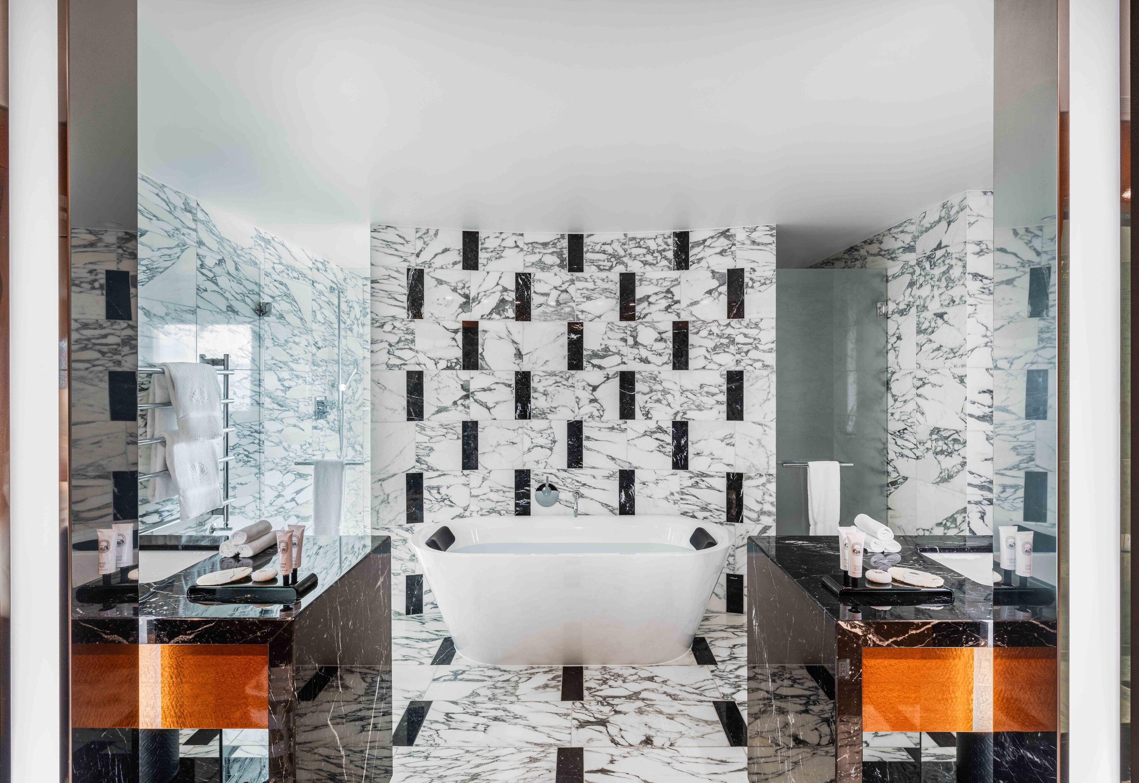 A modern bathroom with a freestanding bathtub, marble walls, and a glass shower enclosure.