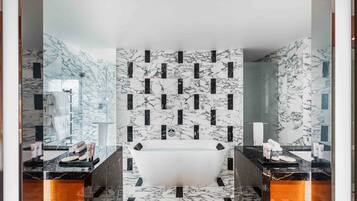 A modern bathroom with a freestanding bathtub, marble walls, and a glass shower enclosure.