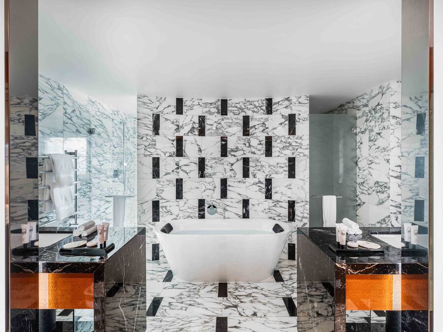 A modern bathroom with a freestanding bathtub, marble walls, and a glass shower enclosure.