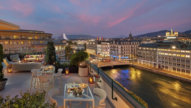 Una terraza en la azotea con asientos al aire libre, una mesa de comedor y vistas al río y al paisaje urbano al atardecer.