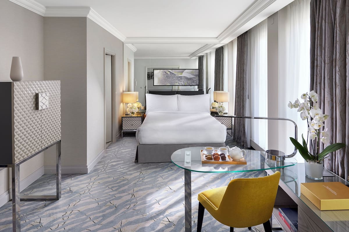 Una habitación de hotel con cama, una mesa de vidrio, una silla, un televisor y una ventana con cortinas.