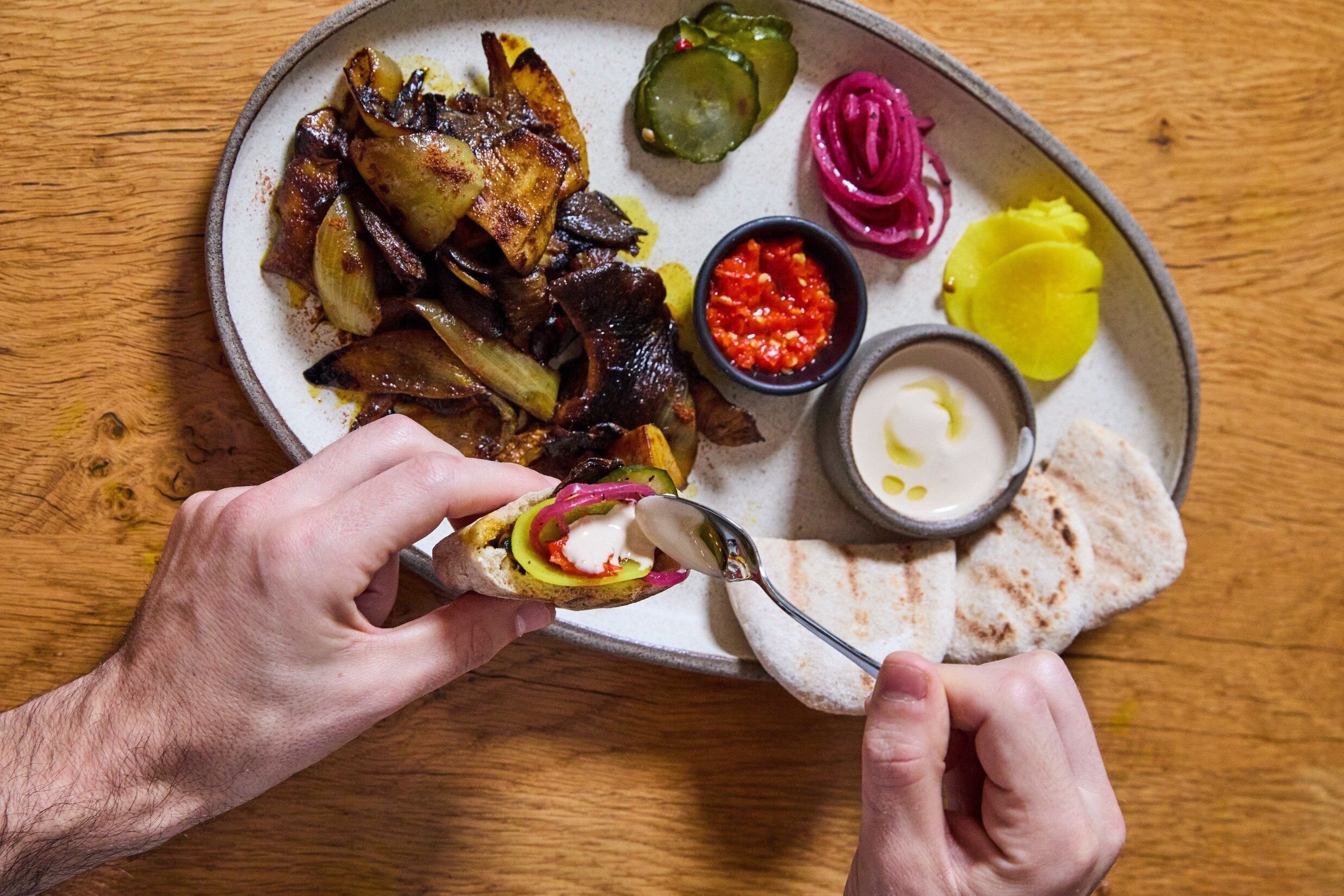 Un plato con carne a la parrilla, verduras y salsas.