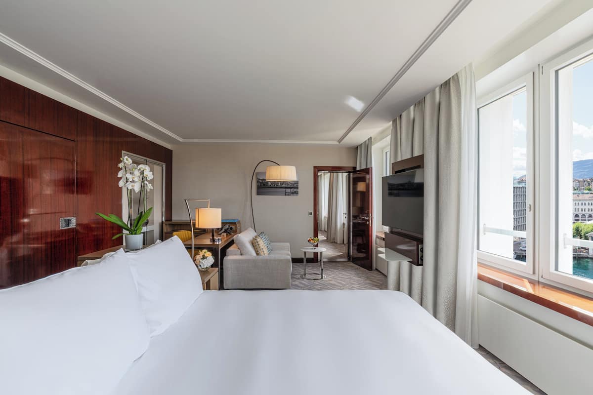 Habitación de hotel con una cama grande, un sofá, una mesita, un televisor y vistas de la ciudad desde la ventana.