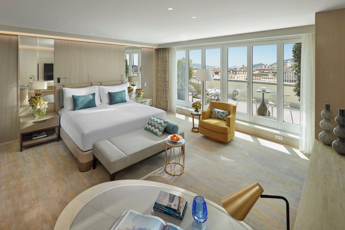Una habitación de hotel moderna con una cama grande, un sofá, una mesa redonda pequeña y un balcón con vistas a la ciudad.