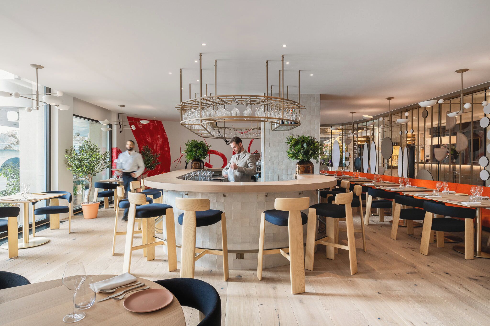 Un restaurante moderno con una barra central, sillas de madera y una combinación de mesas dentro y fuera.
