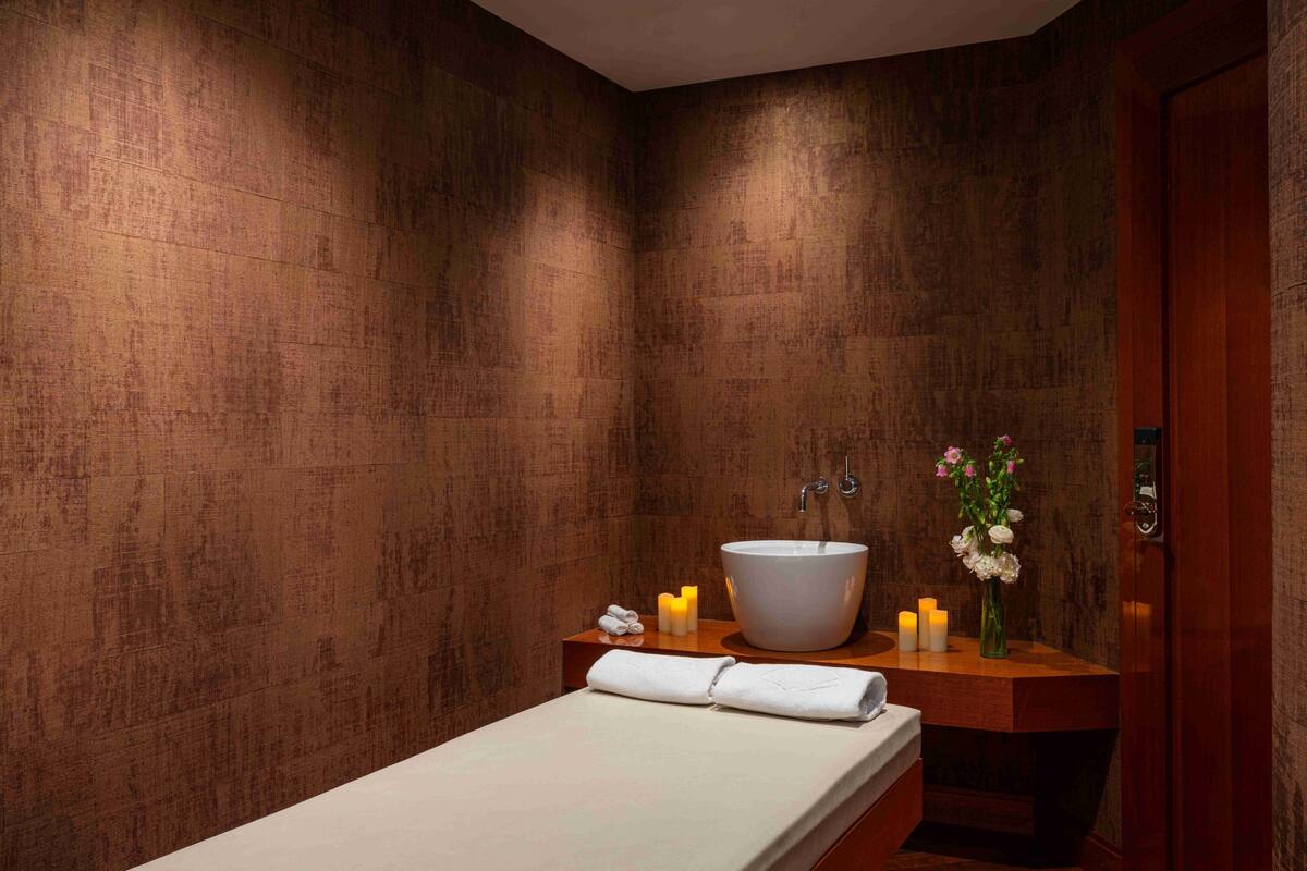 A modern bathroom with a large vessel sink, wooden vanity, and a bed with a white towel.