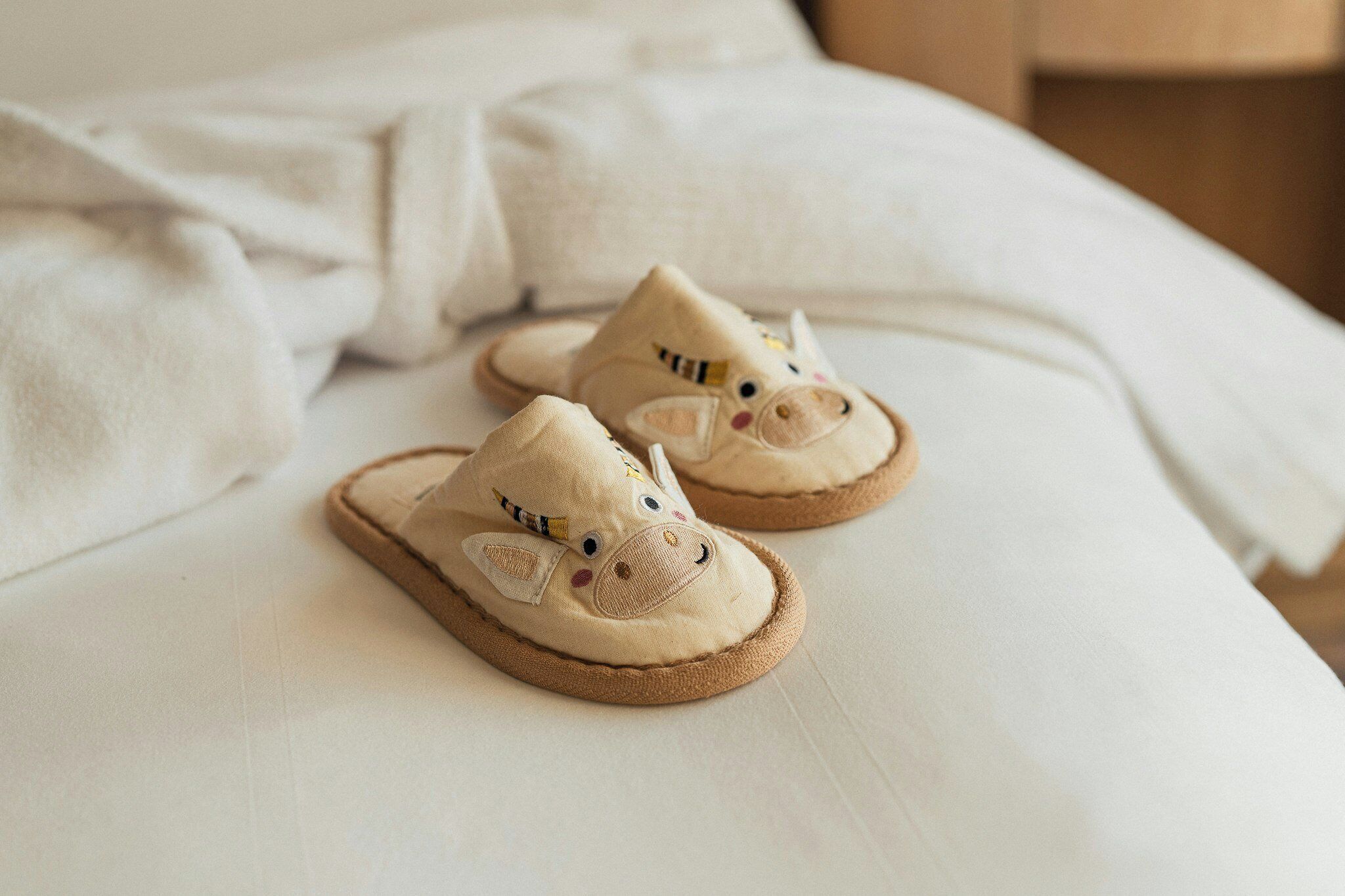 A pair of animal-themed slippers on a bed.
