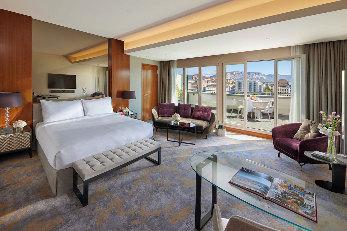 Habitación de hotel con una cama grande, un sofá, una mesa de centro de vidrio y vistas a la ciudad.