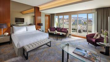 A hotel room with a large bed, a sofa, a glass coffee table, and a view of the city.