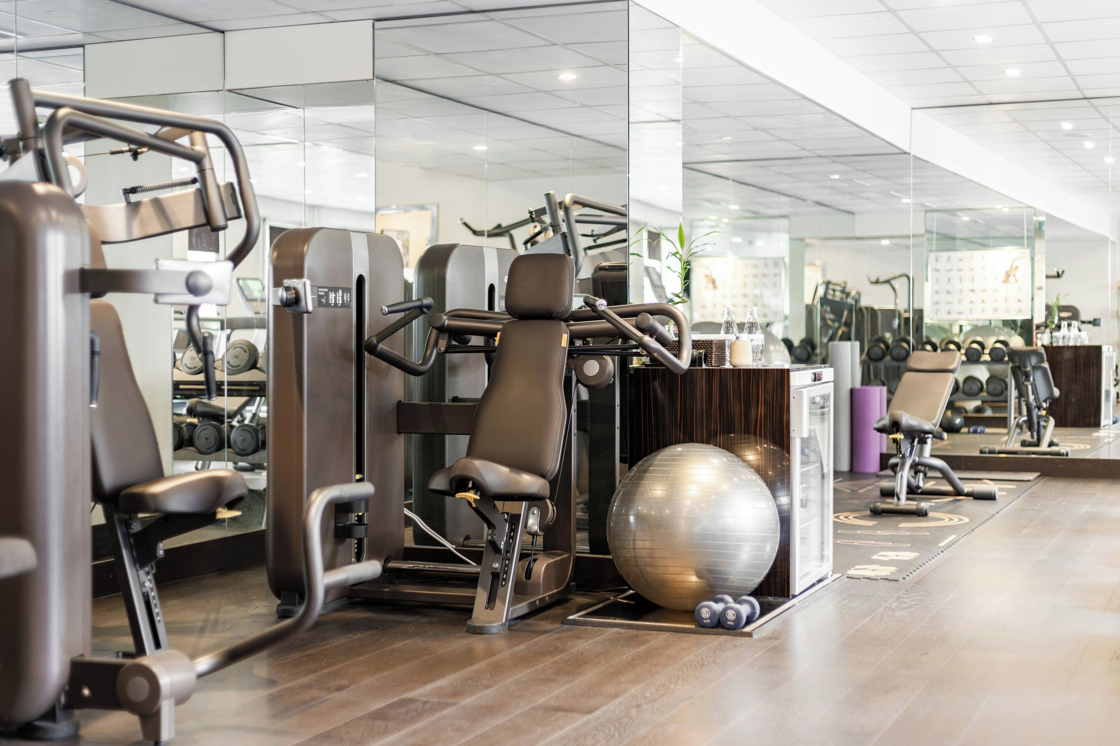 Un gimnasio con equipo de ejercicio, un muro espejado y piso de madera.