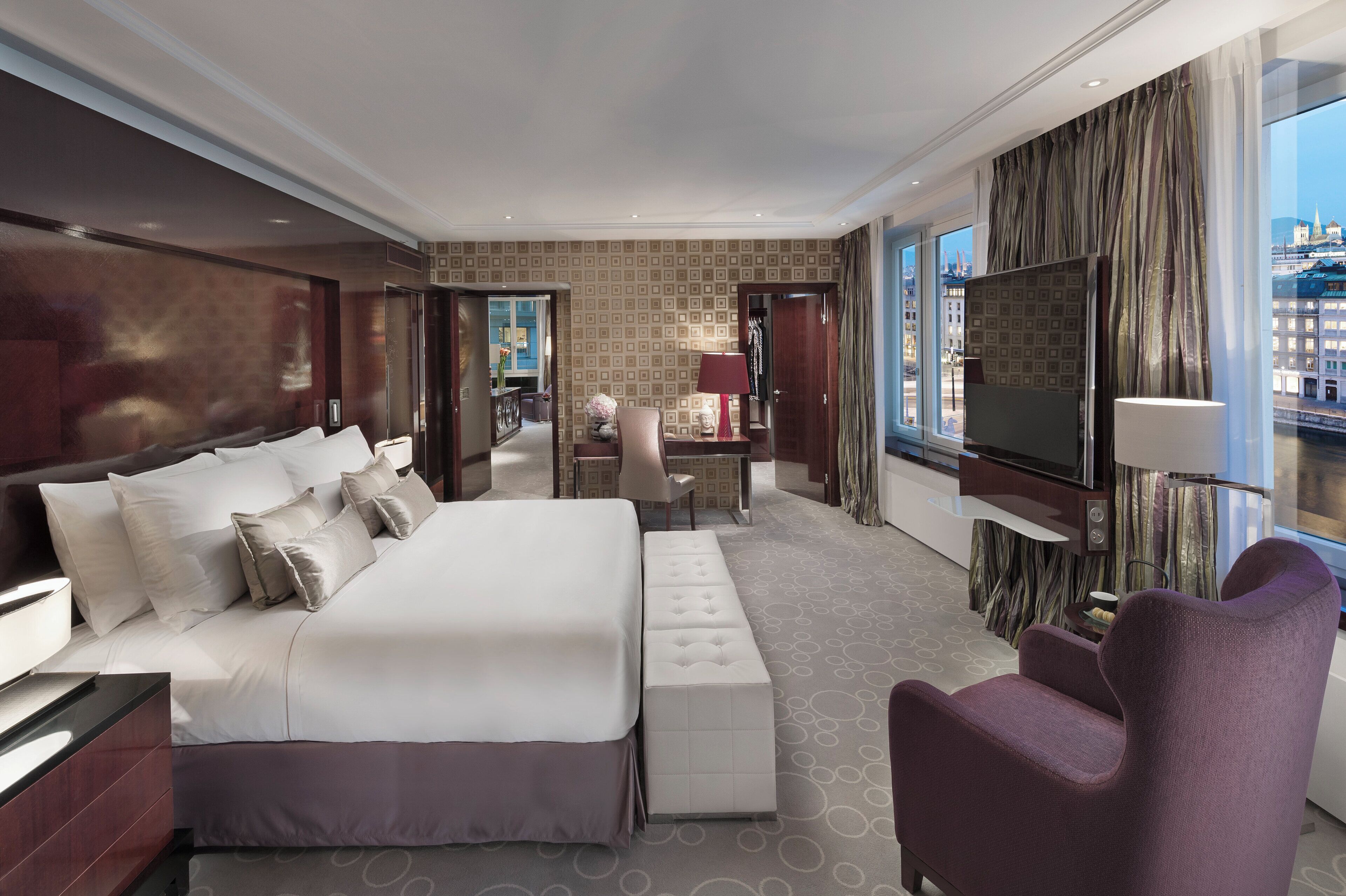 A modern hotel room with a large bed, a desk, a chair, and a TV.