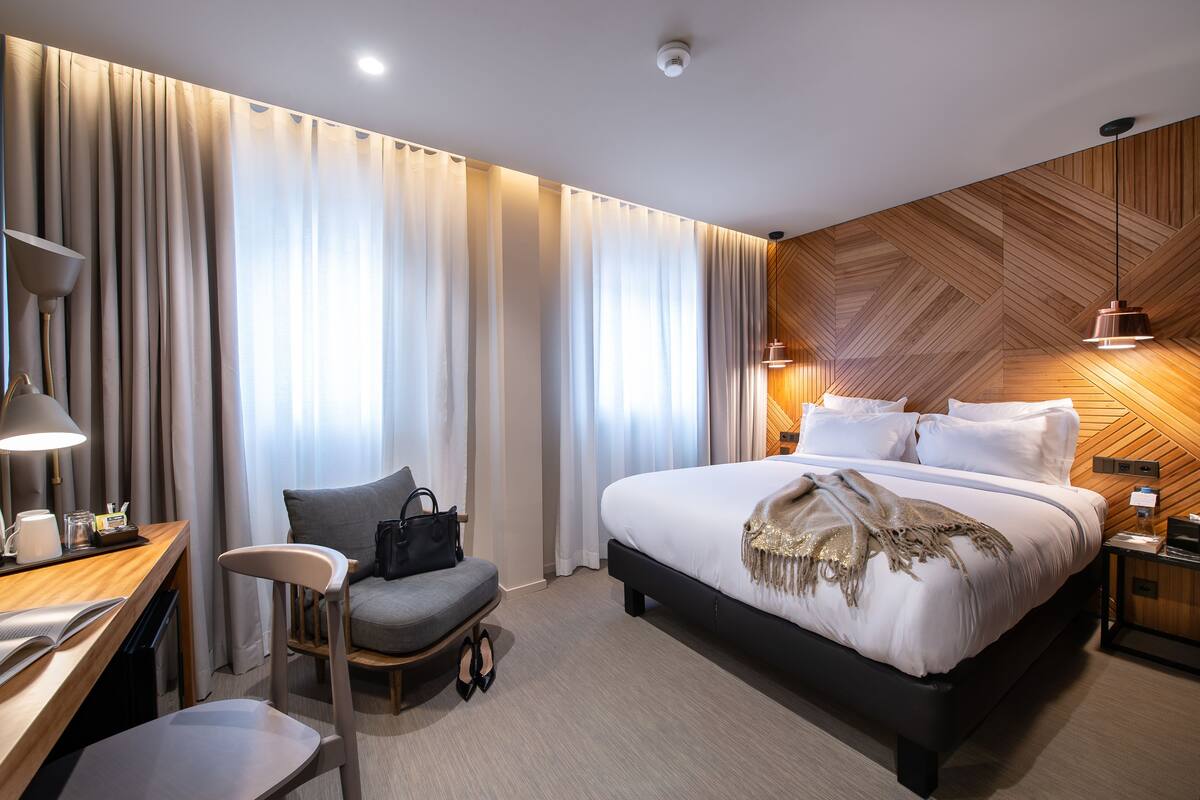 Moderni hotellihuone, jossa on suuri sänky, työpöytä lampun kanssa, tuoli ja vaatekaappi.