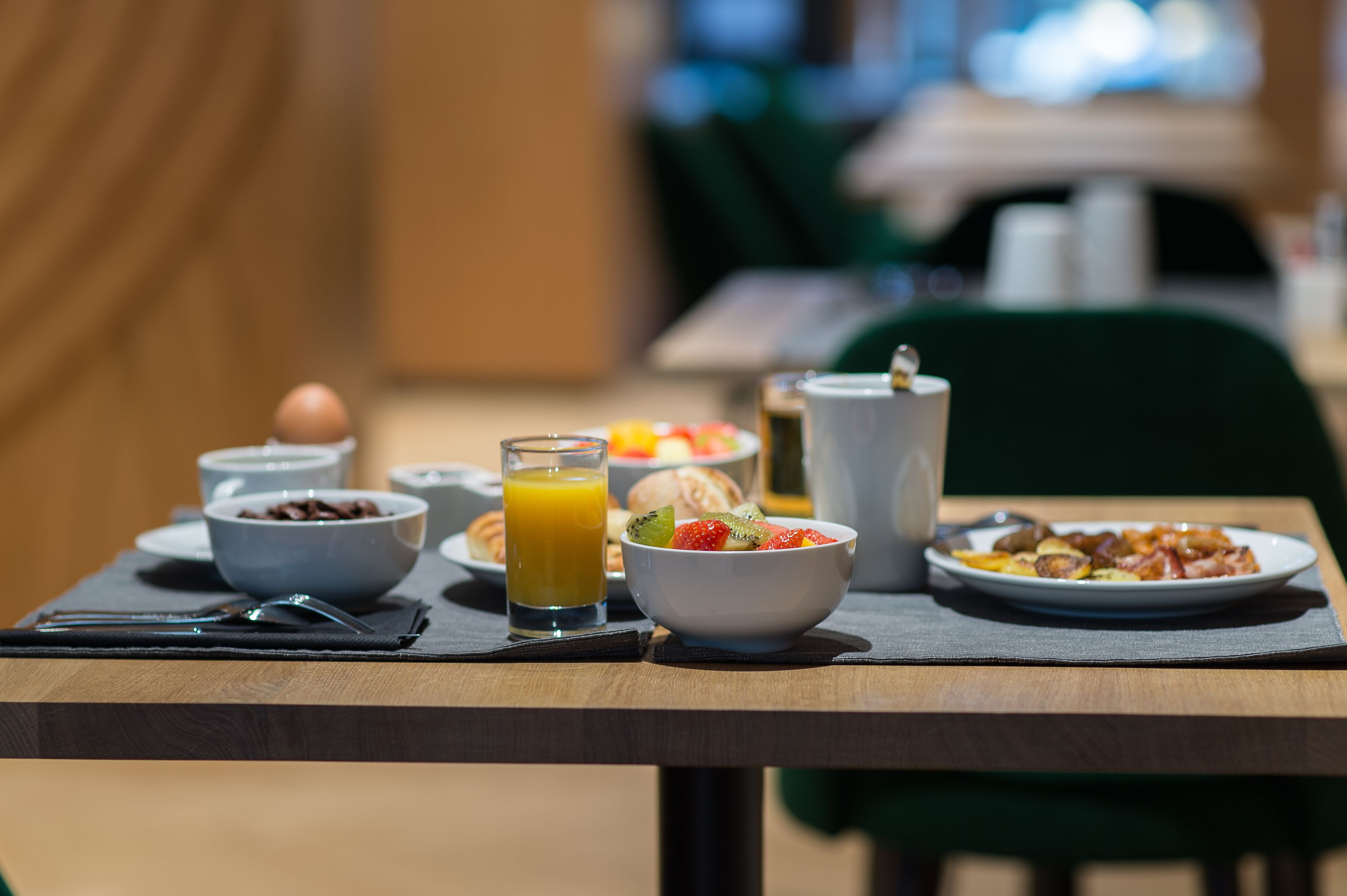 Une table de petit-déjeuner avec des bols de céréales, un verre de jus d’orange et des assiettes remplies de nourriture.