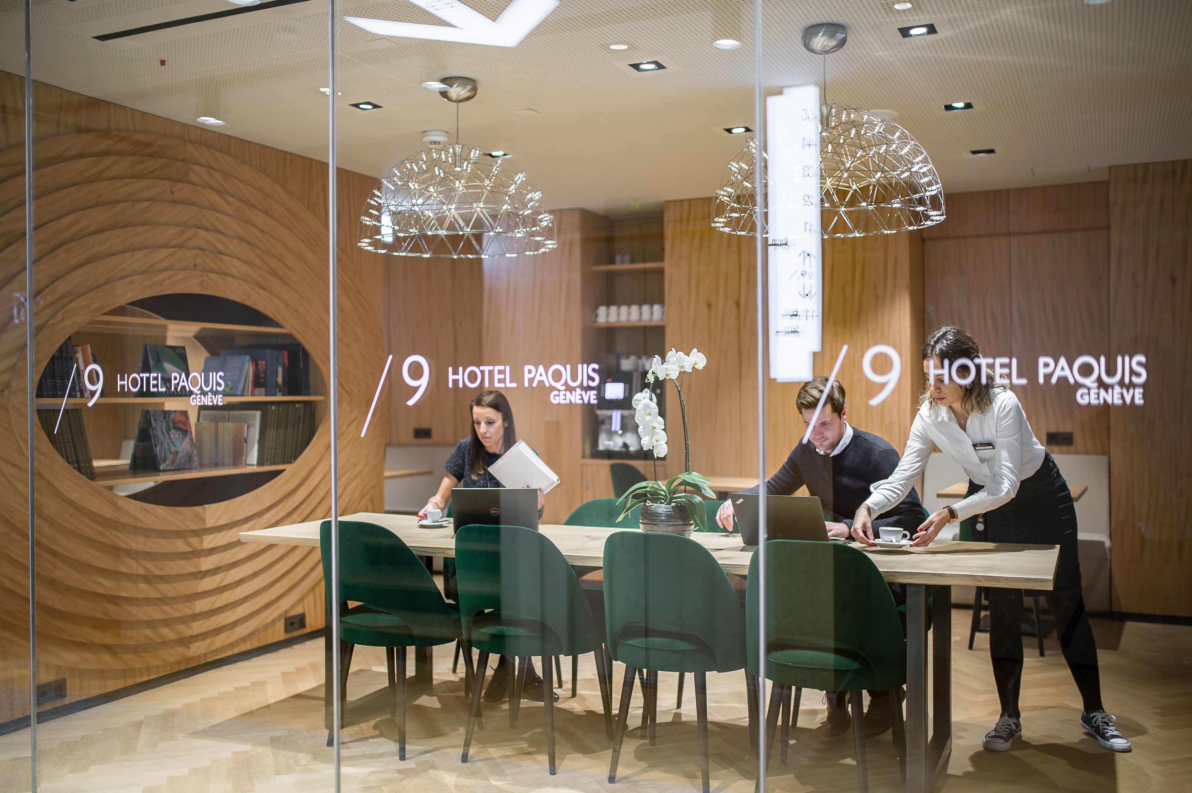 Un moderno vestíbulo de hotel con una pared curva de madera, una recepción y una zona de estar con sillas verdes.