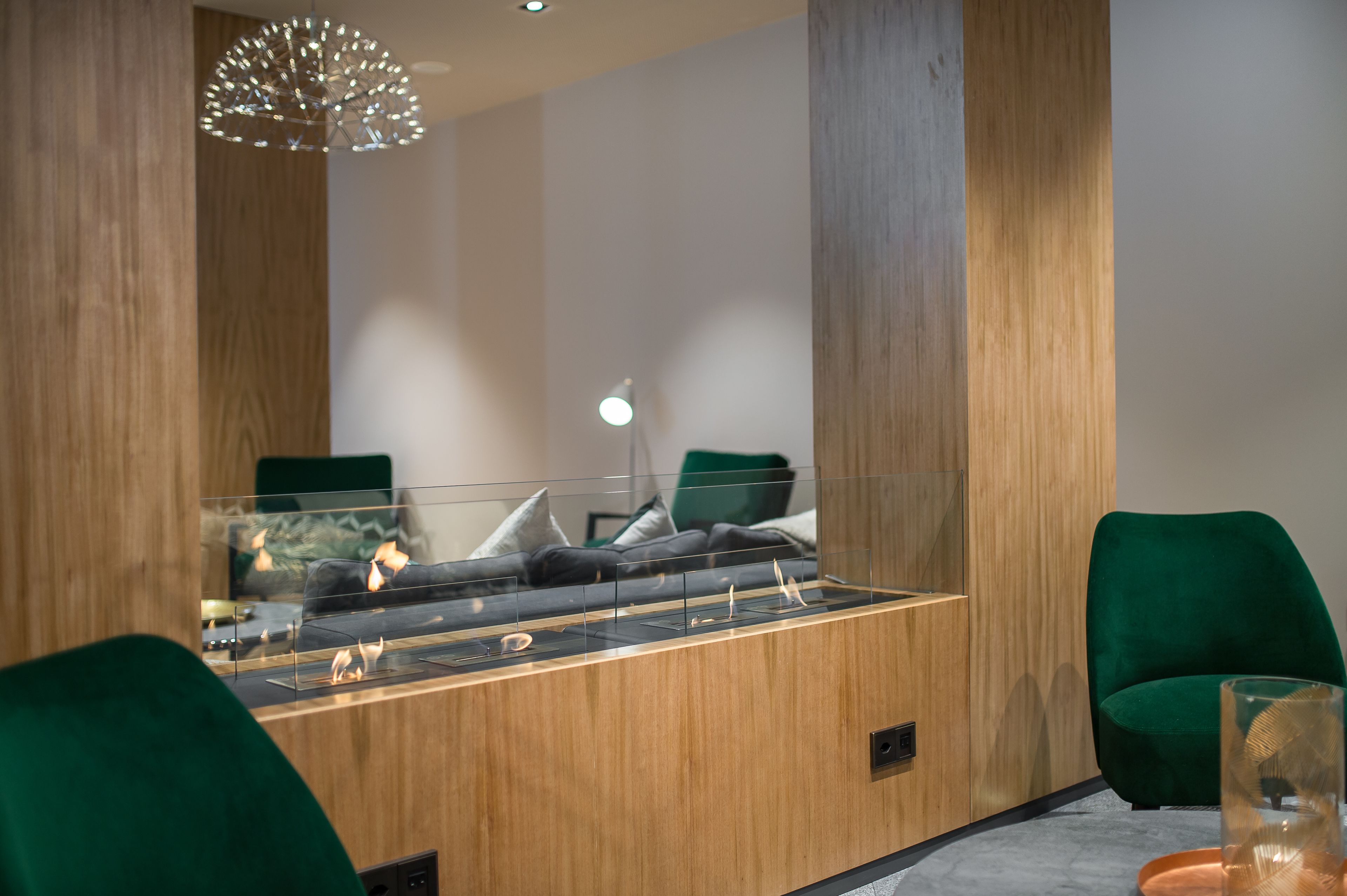 A modern room with a wooden reception desk, a glass partition, a green chair, and a unique chandelier.