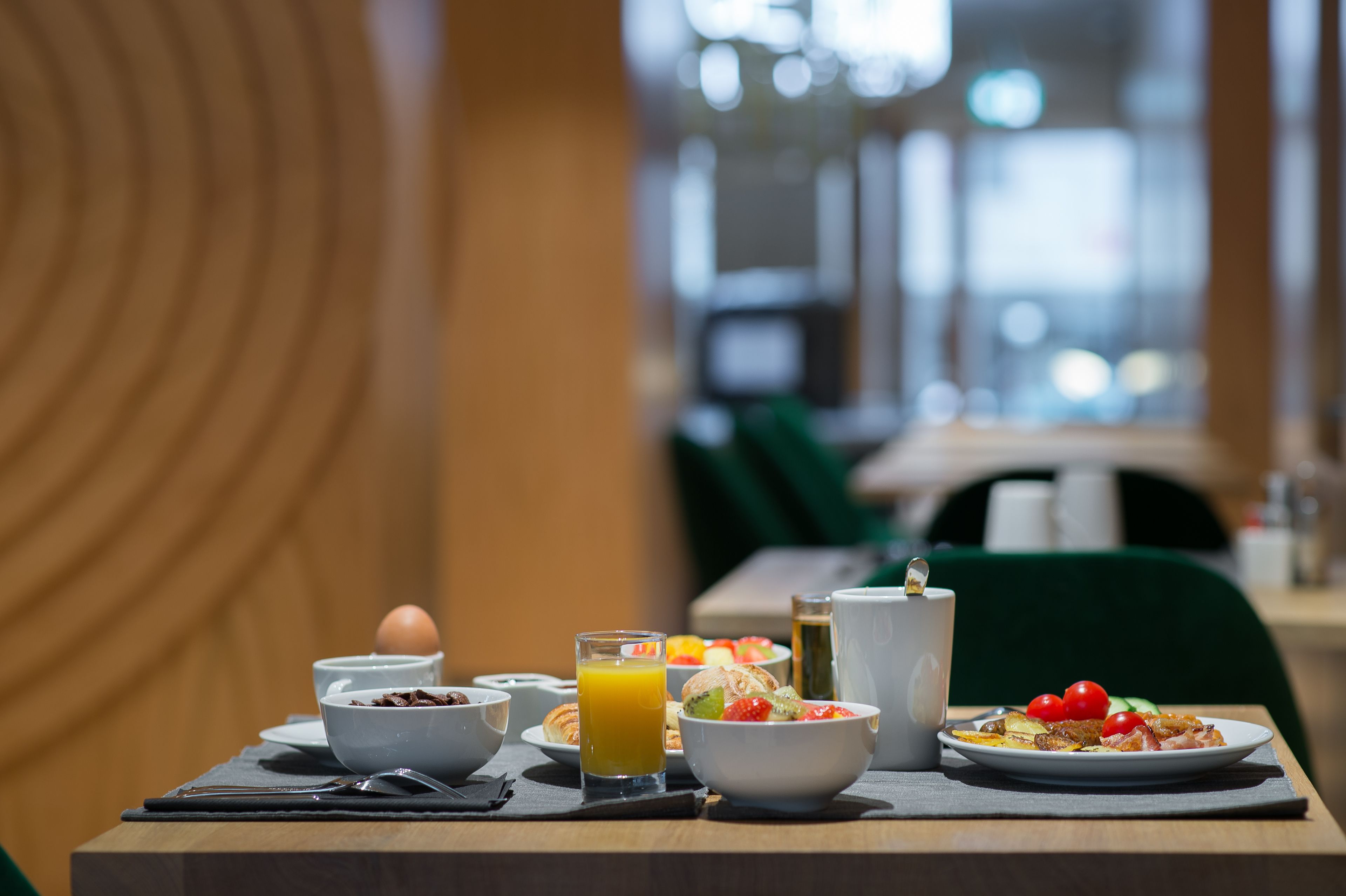 Une table dressée pour le petit-déjeuner, avec différents plats, un verre de jus d’orange et une tasse.