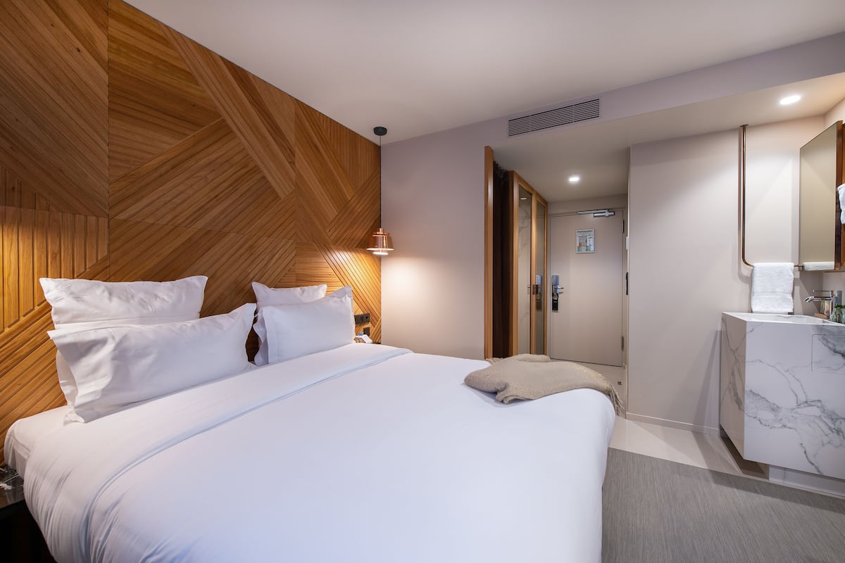 Moderni hotellihuone, jossa on puukoristeinen seinä, suuri sänky valkoisilla vuodevaatteilla, marmorinen kylpyhuoneen allas ja erillinen vaatehuone.