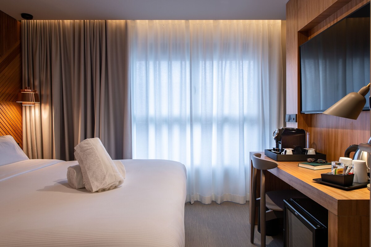 Hotellihuone, jossa on sänky, työpöytä, kahvinkeitin ja televisio.