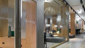 Un interior de hotel moderno con paredes de vidrio, paneles de madera y una lámpara araña contemporánea.