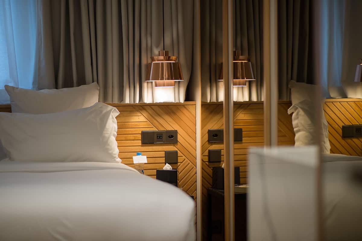 Hotellihuone, jossa on kaksi sänkyä, puupanelointi, peili ja yöpöytä, jossa on lamppu.