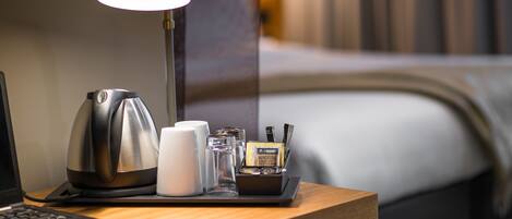 Un escritorio de hotel ordenado con tetera, tazas, lámpara y una bandeja pequeña con artículos de aseo.