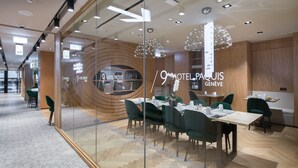 Un moderno vestíbulo de hotel con un separador de vidrio, paneles de madera y un comedor con sillas verdes y una mesa de madera.
