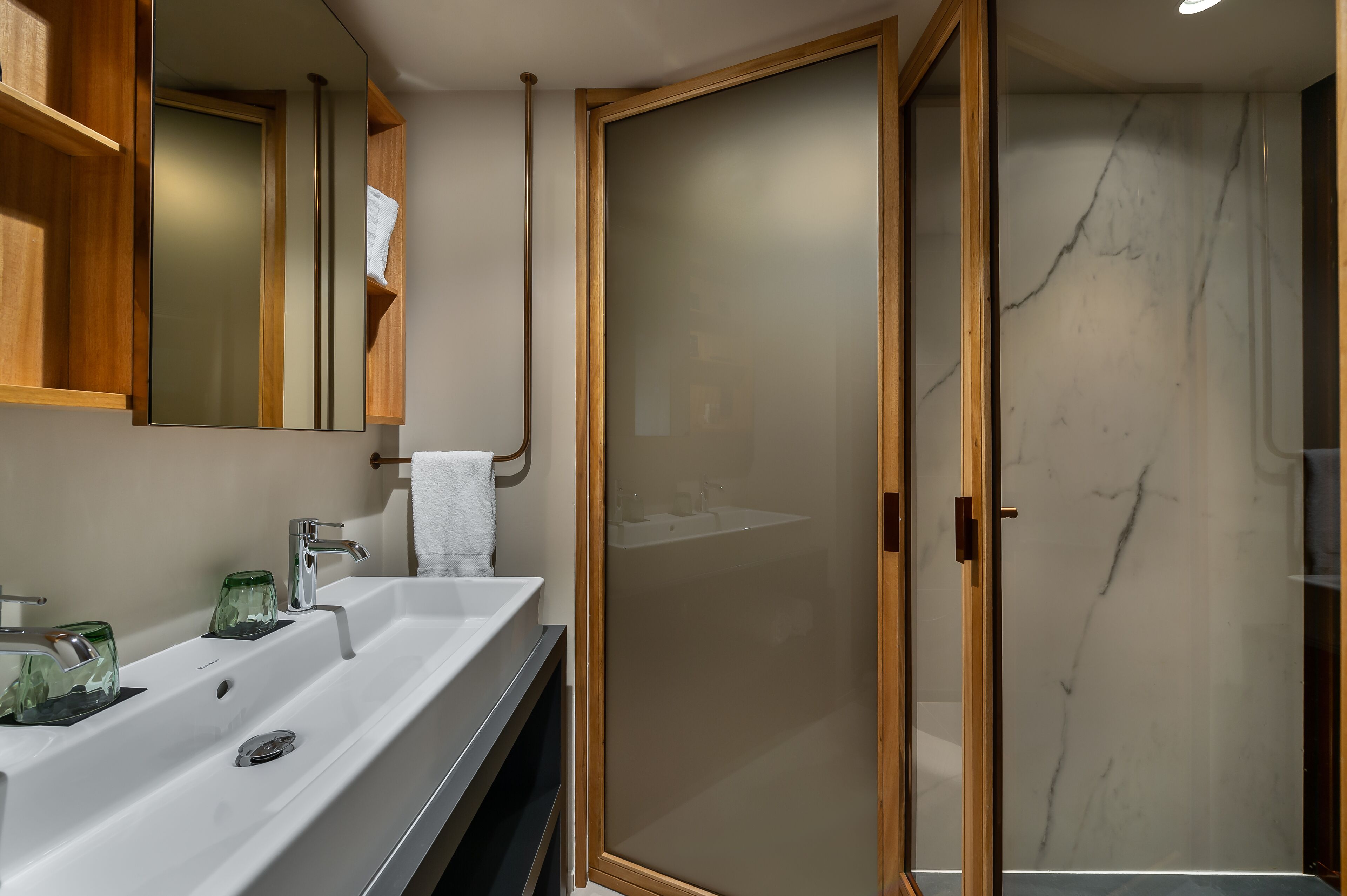 Un baño moderno con un espejo grande, un lavabo blanco y una ducha con mampara de vidrio.
