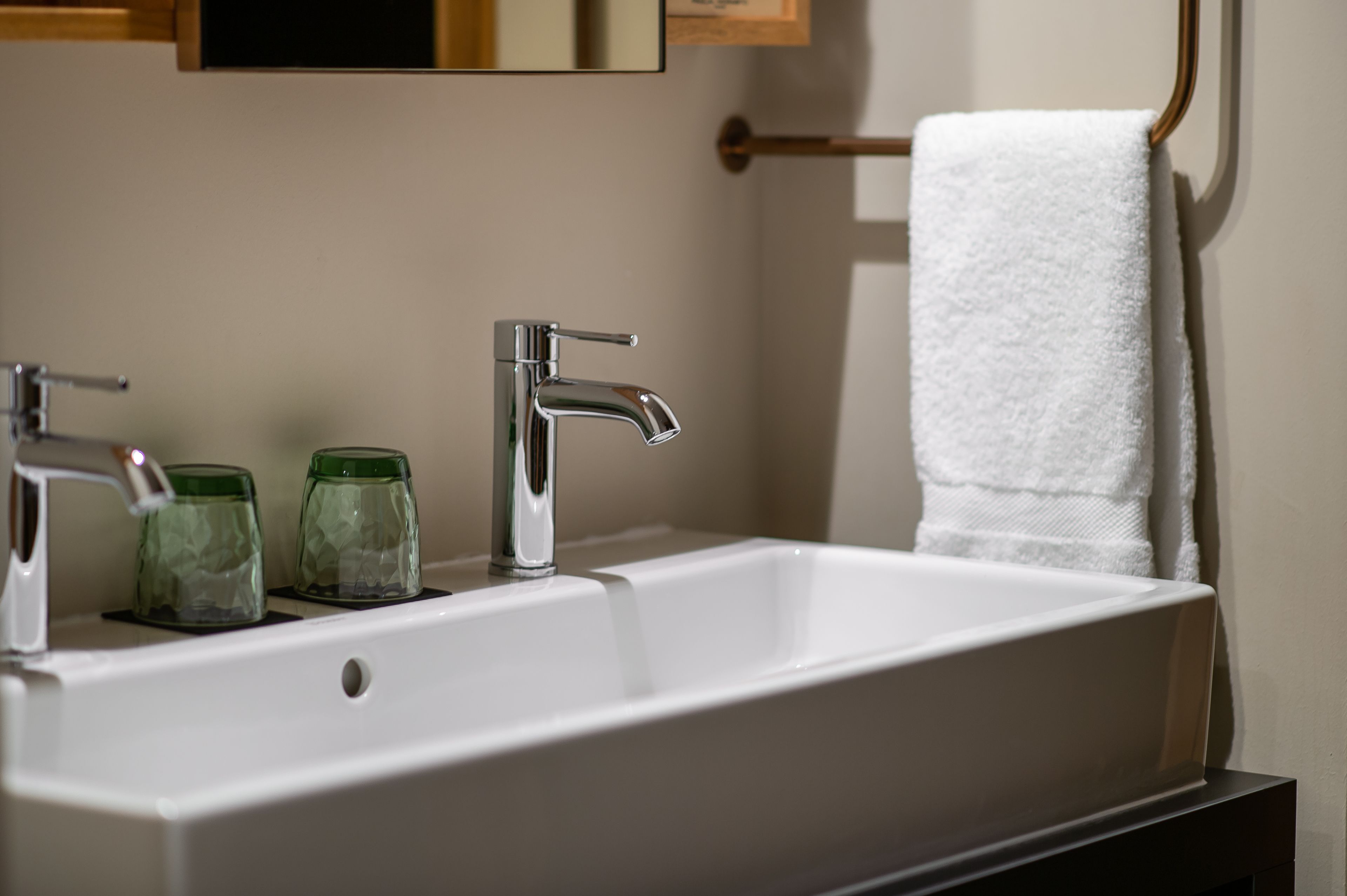 A bathroom with a white sink, two green glass jars, a white towel, and a mirror above the sink.