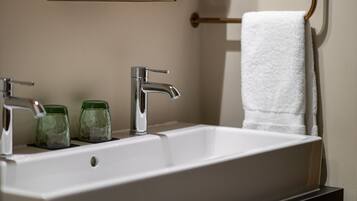 A bathroom with a white sink, two green glass jars, a white towel, and a mirror above the sink.
