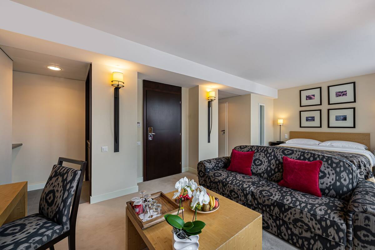 A hotel room with a sofa, a coffee table with a tray of snacks, a chair, and a door.