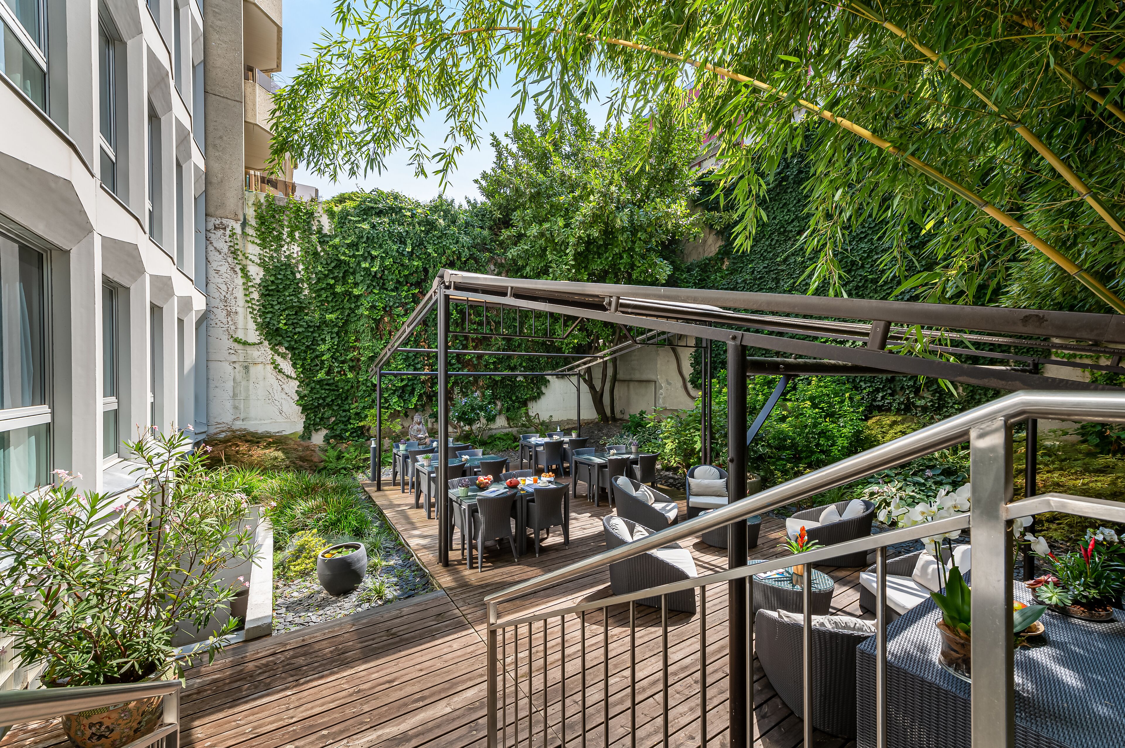 A rooftop patio with outdoor seating, surrounded by lush greenery and a view of a building.