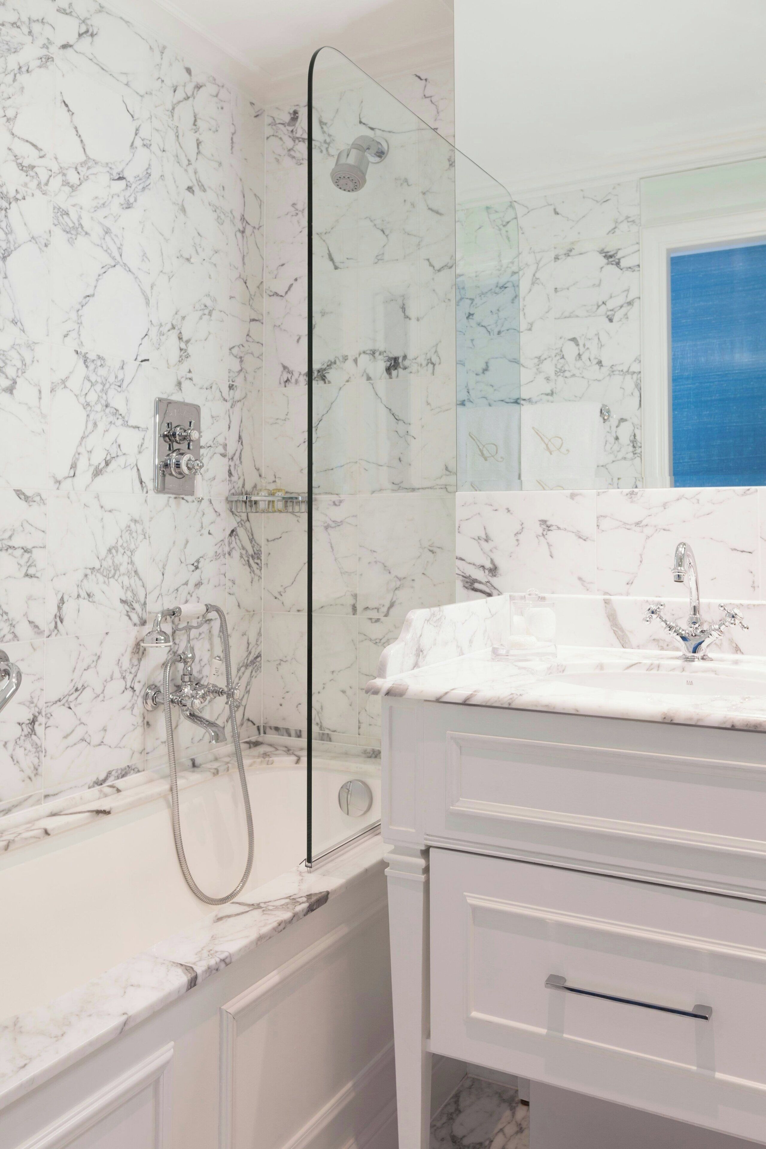 A bathroom with a marble wall, a glass shower enclosure, a bathtub, and a vanity with a mirror.