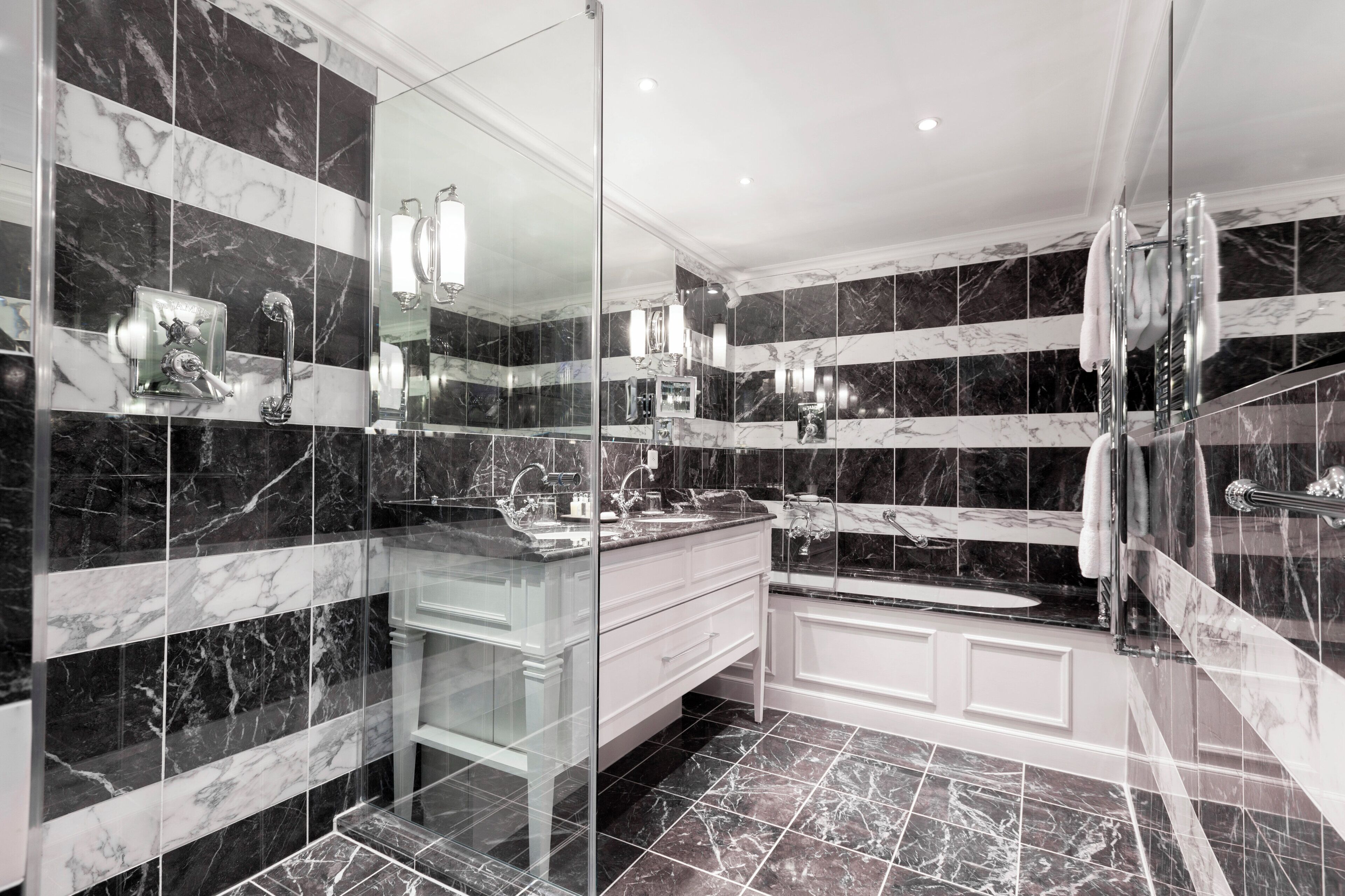 Un baño moderno con paredes de mármol, ducha con mampara de vidrio y tocador con lavabo y espejo.