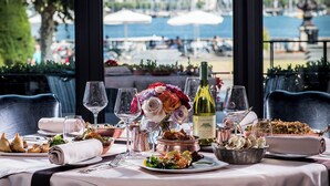 A table set with various dishes, wine glasses, and a bottle of wine, overlooking a marina with boats and umbrellas. - Hotel d'Angleterre Geneva (Geneva)